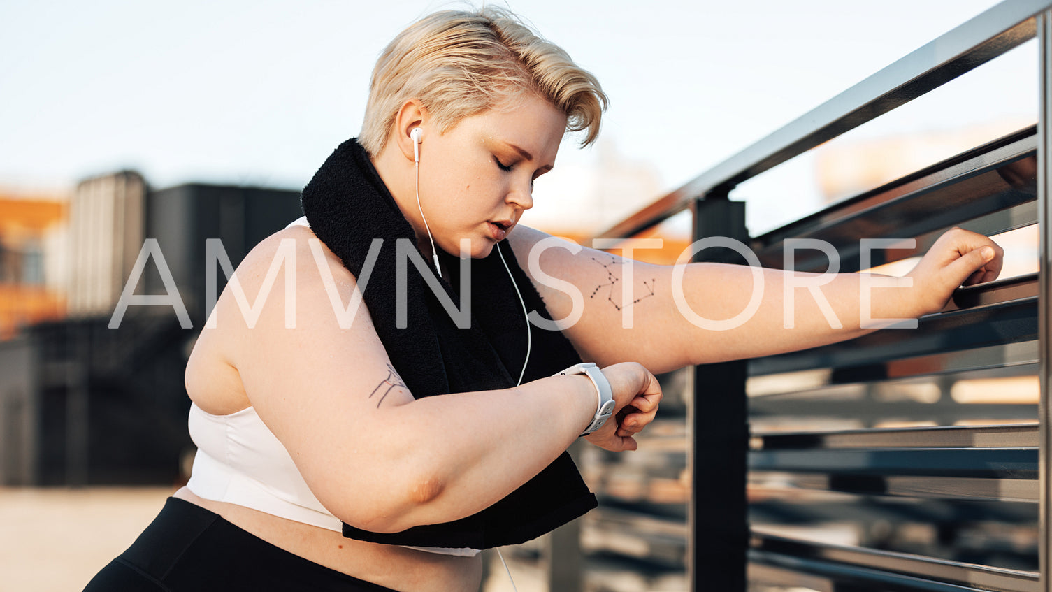 Side view of young plus-size woman looking at a smartwatch. Sweated and exhausted curvy woman with a towel around her neck relaxing during training.	