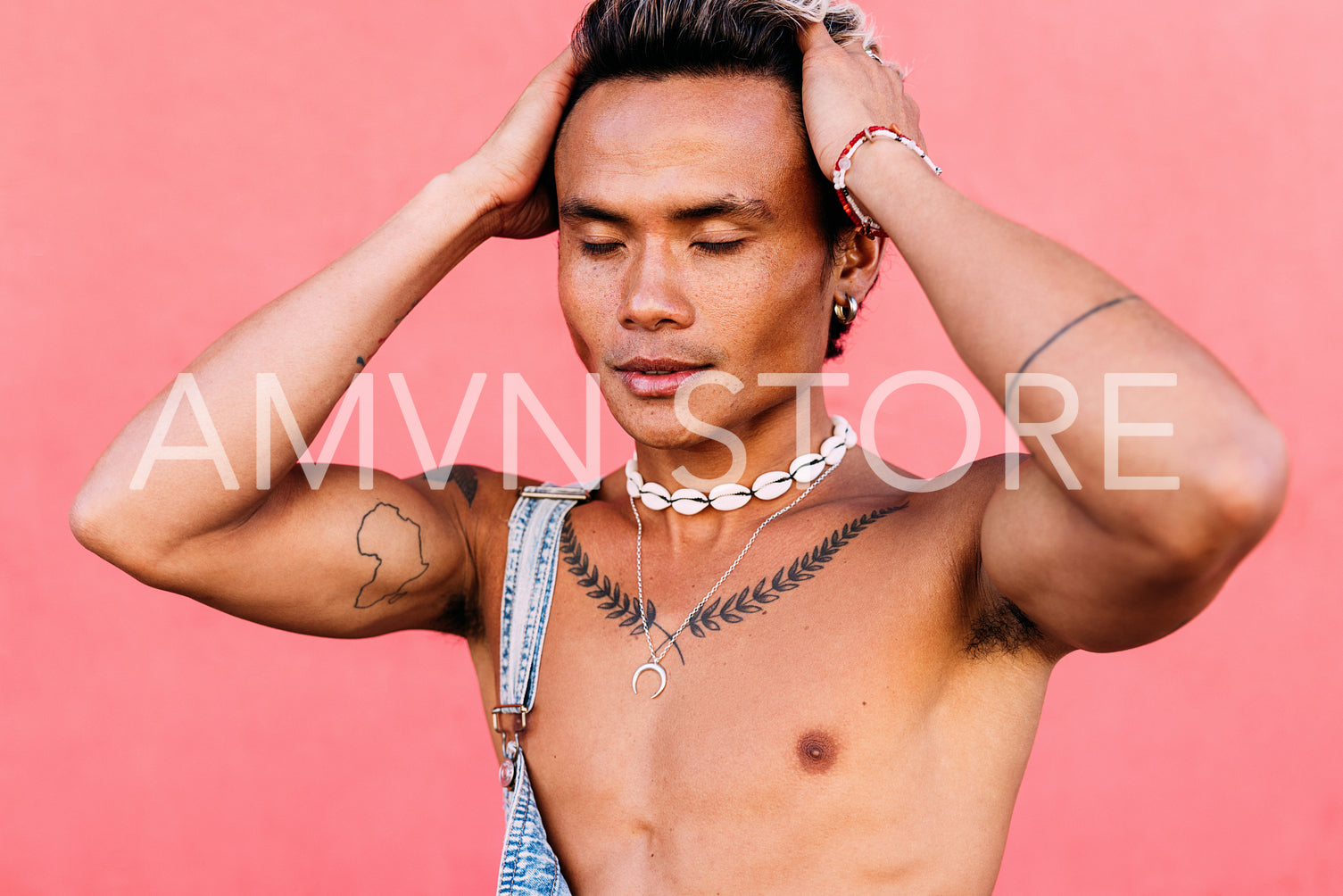 Close up of a young man with tattoos standing against pink wall with closed eyes