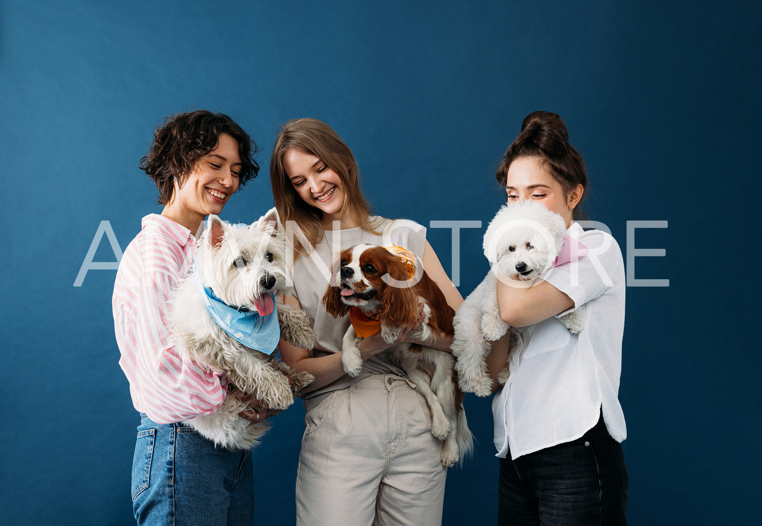 Three young women holding their cute little dogs while standing 