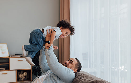 Smiling father lifting his son while sitting on a sofa at home.