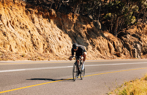 Professional sportsman riding his bicycle on an empty road in wild terrain. Male cyclist practicing riding on bicycle.