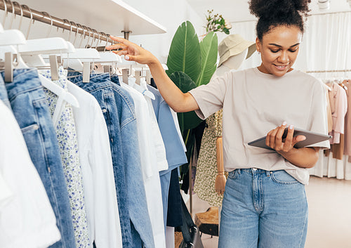 Young boutique owner taking inventory standing at rack with digital tablet