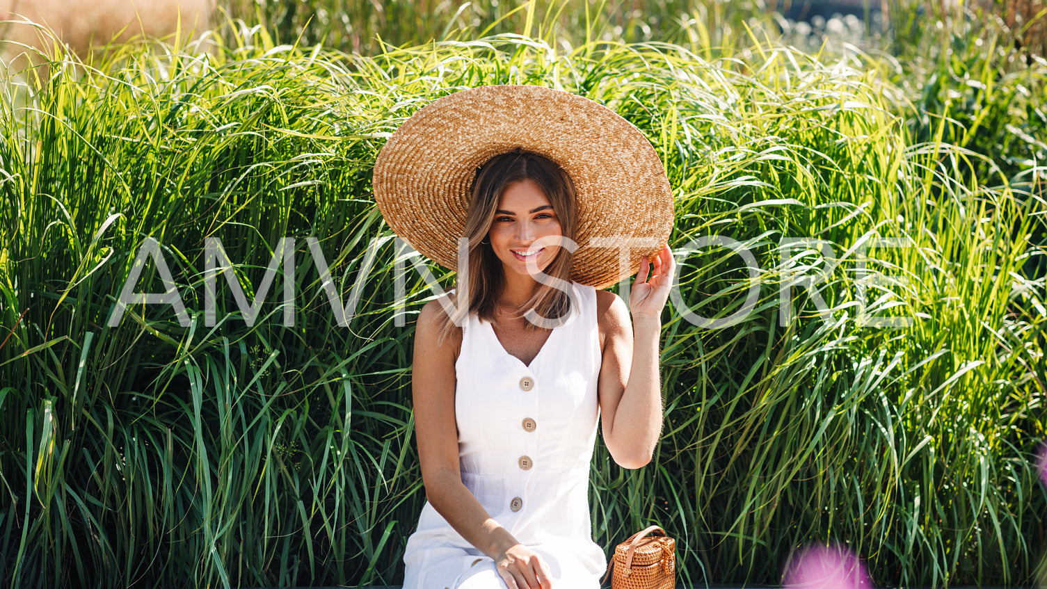 Beautiful blond woman holding her sun hat and looking at camera in the park	