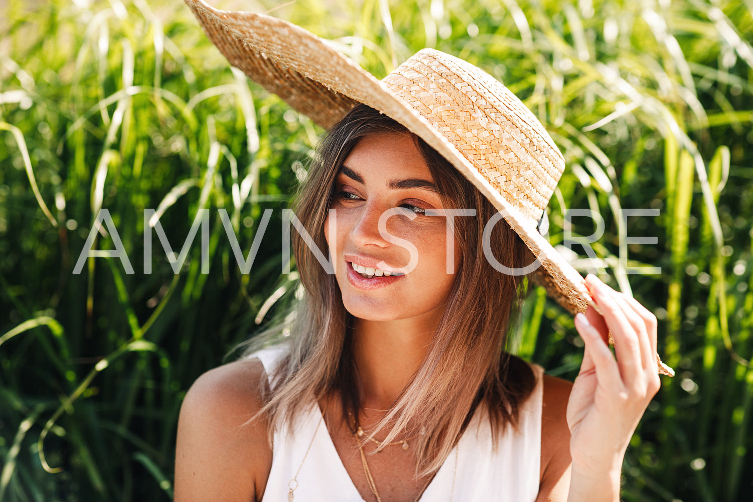 Young smiling woman wearing straw hat while sitting in park in front of a grass	