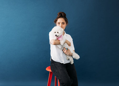 Young woman hugging her little white dog in studio while sitting