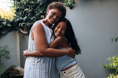 Smiling girl hugging her granny in the backyard. Grandmother and granddaughter are embracing with closed eyes.