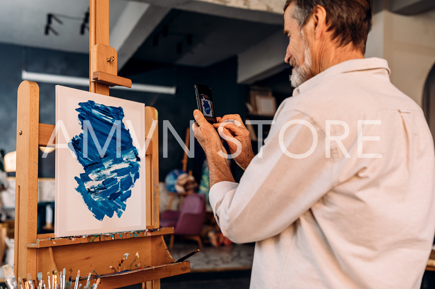 Artist photographing his abstract picture on mobile phone in workshop	