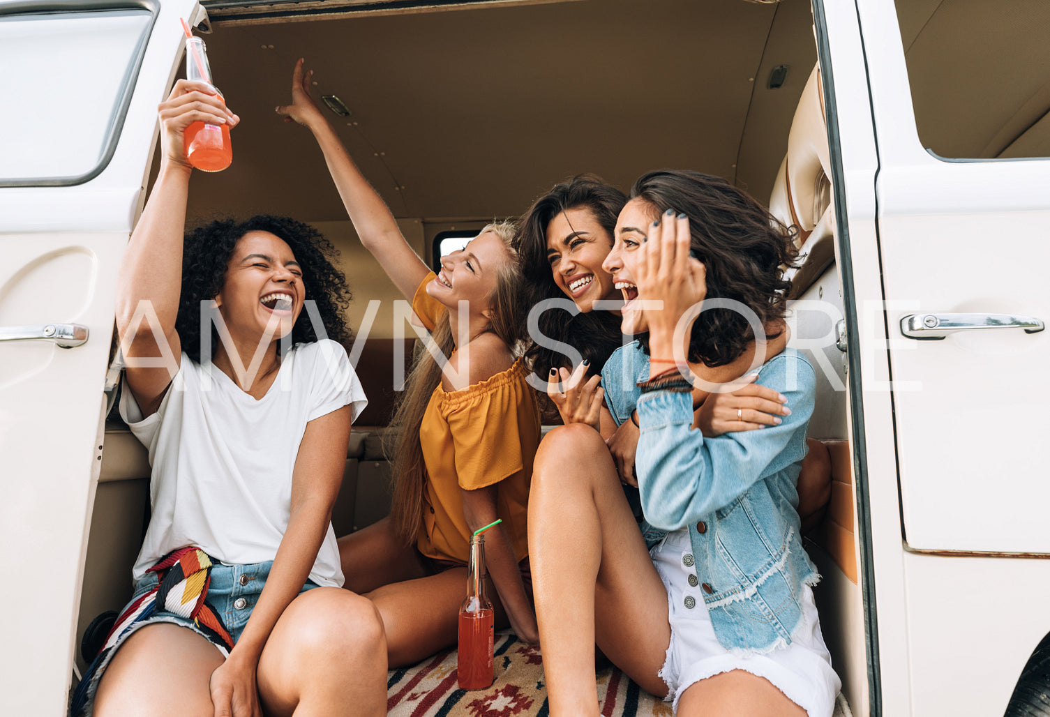 Multi ethnic group of women hanging out during road trip. Friends in van raising hands and laughing.