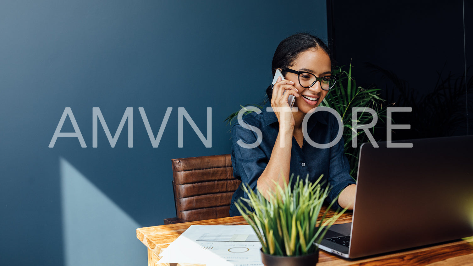 Entrepreneur sitting at table typing on a laptop while talking on cell phone	