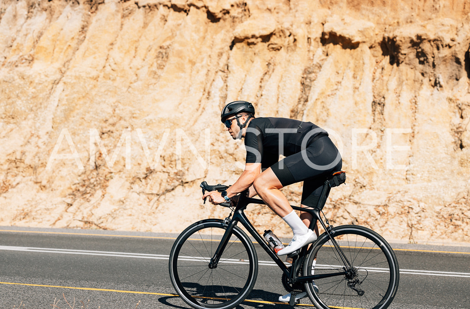 Professional triathlete in black sportswear riding road bike a hill on an empty road