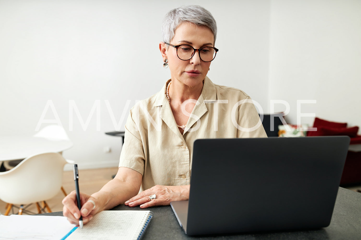 Mature woman looking at laptop screen making notes at home