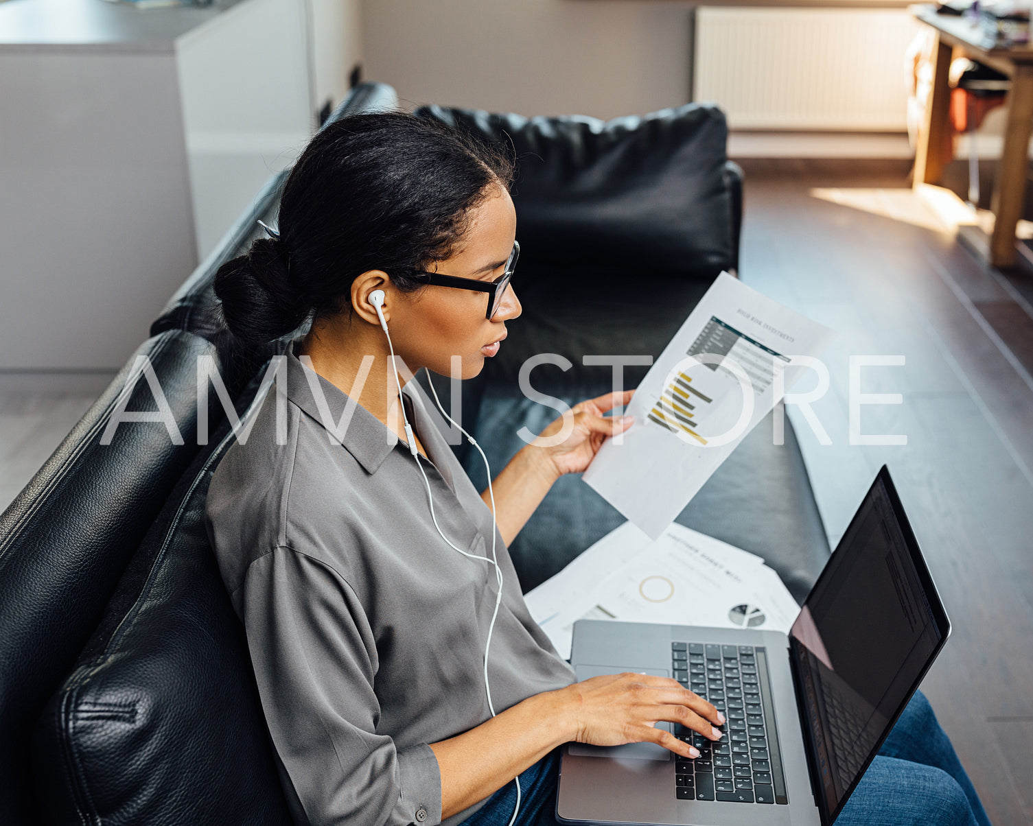 Young woman holding documents and typing on laptop computer while sitting on sofa	