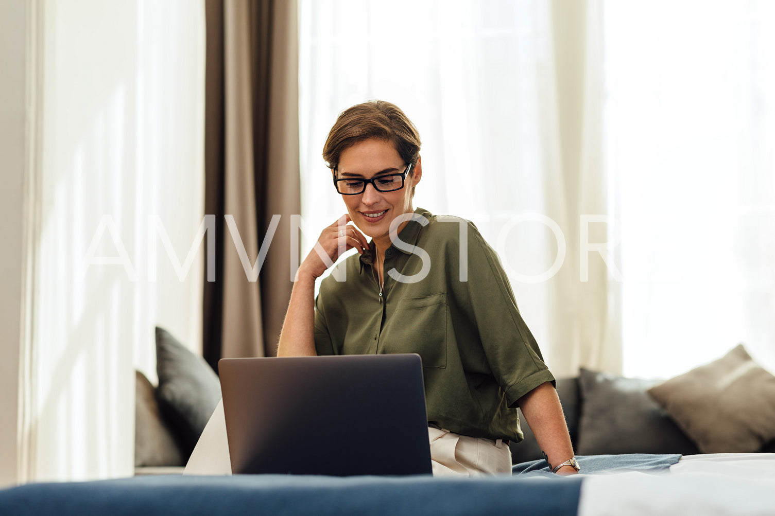 Business woman in modern hotel room sitting on bed using laptop and smiling	