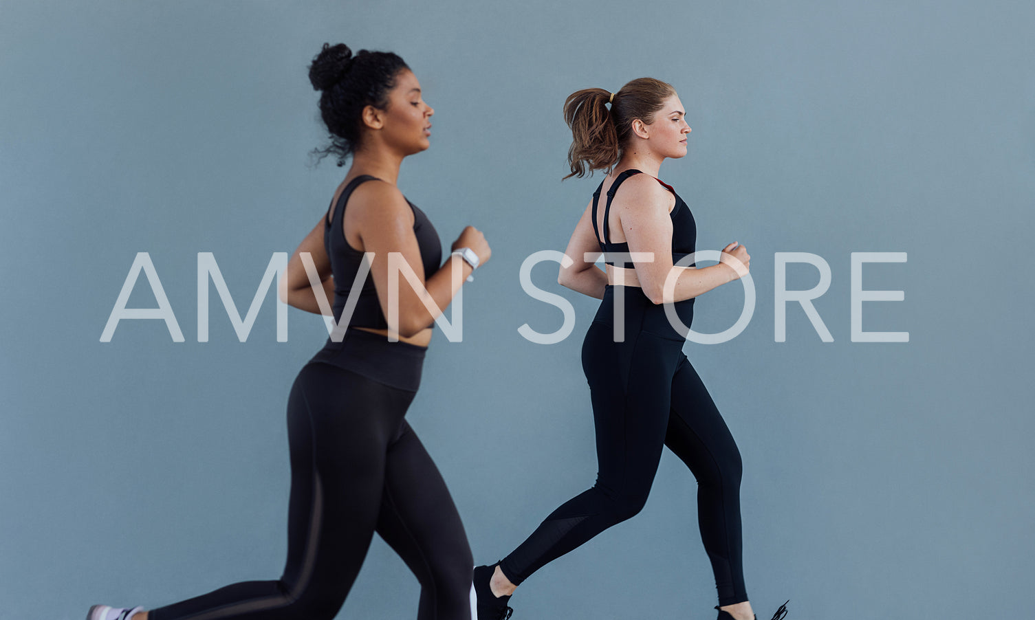 Side view of two plus size females running at grey wall. Two women in black fitness attire jogging outdoors.