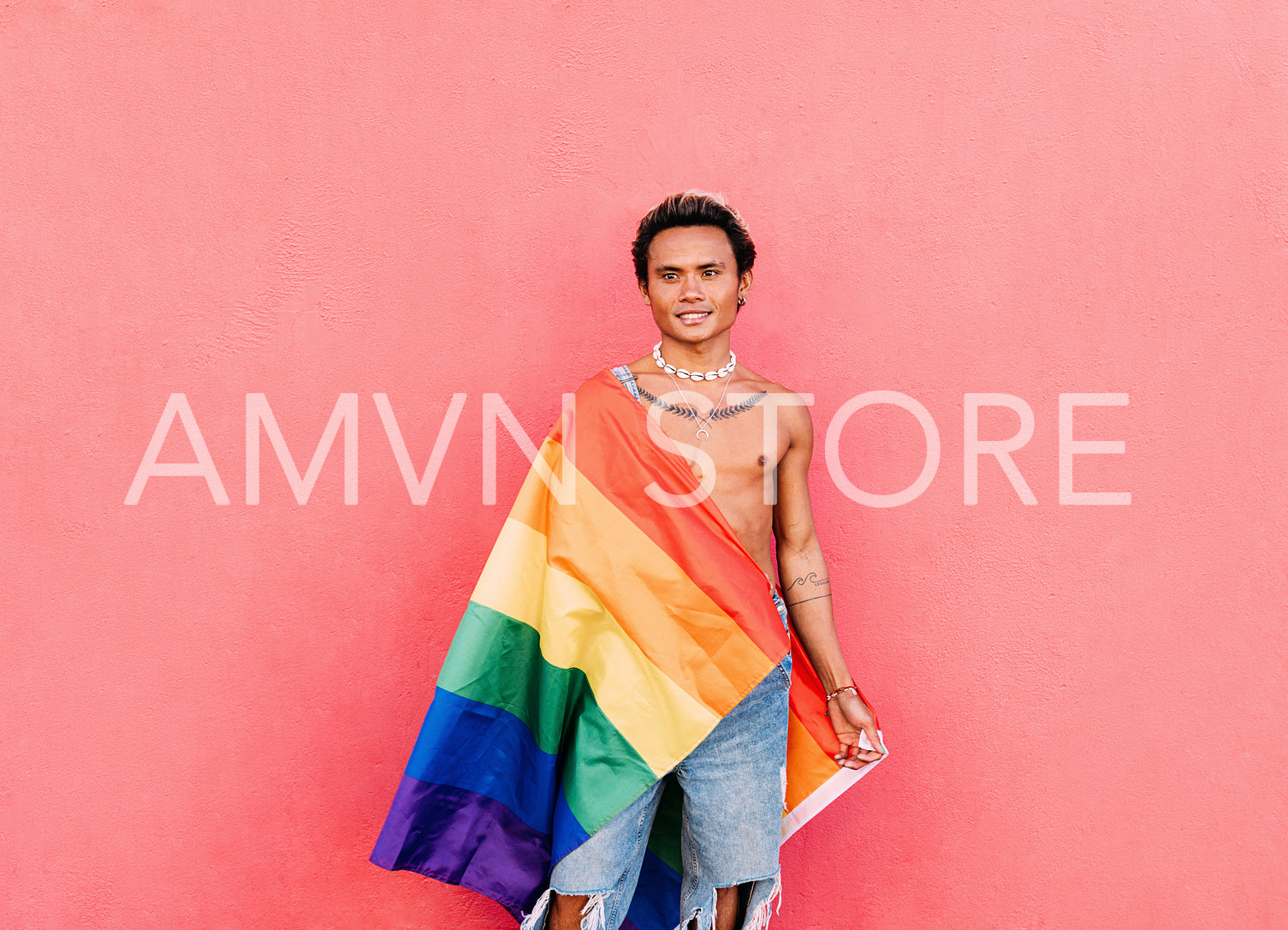 Young handsome man wrapped in rainbow LGBT flag at pink wall