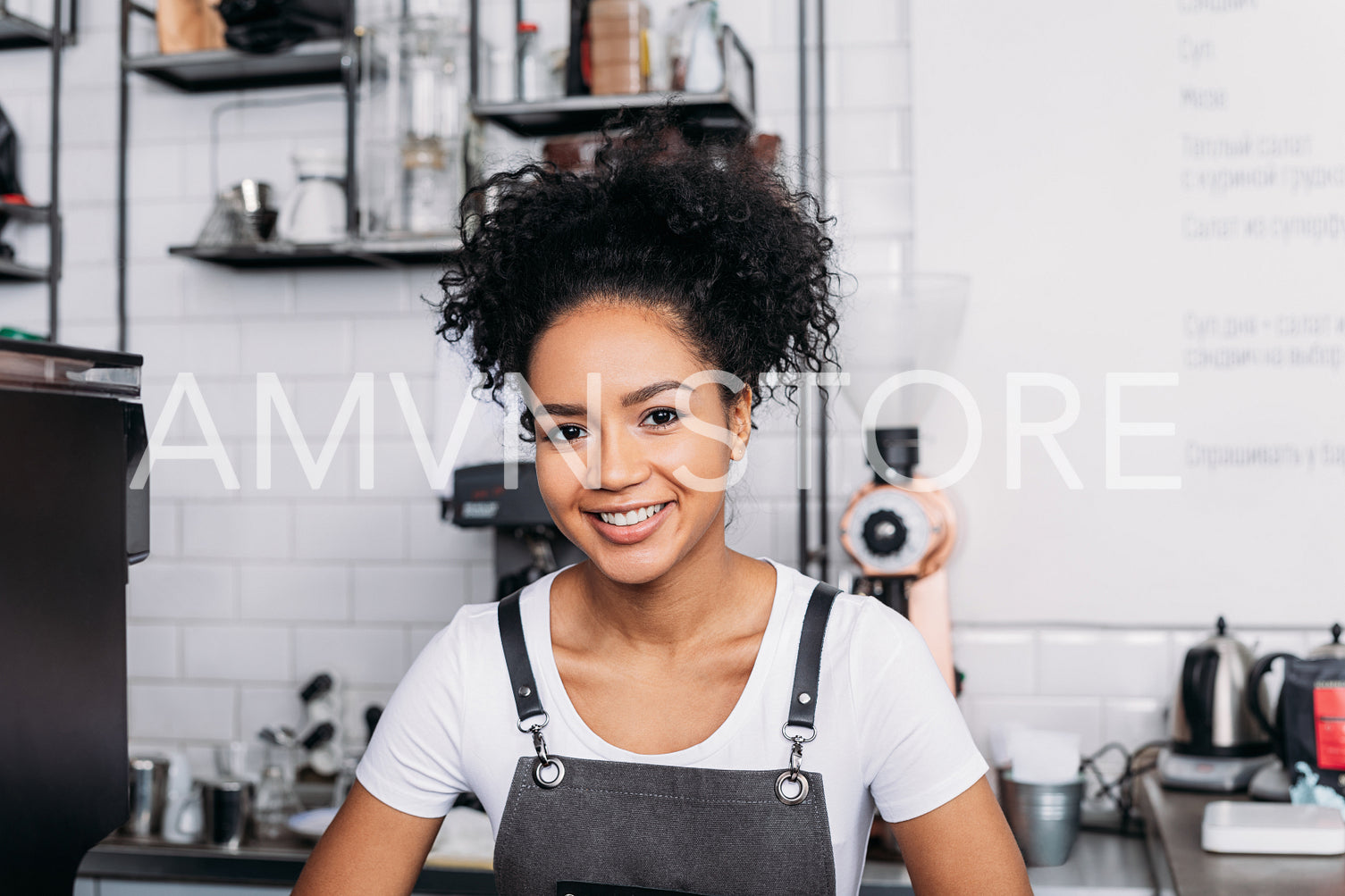 Close-up of a young smiling barista with curly hair wearing an apron