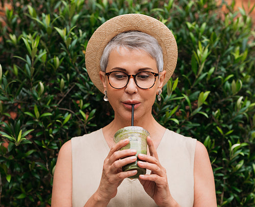 Aged woman with short hair drinking a smoothie