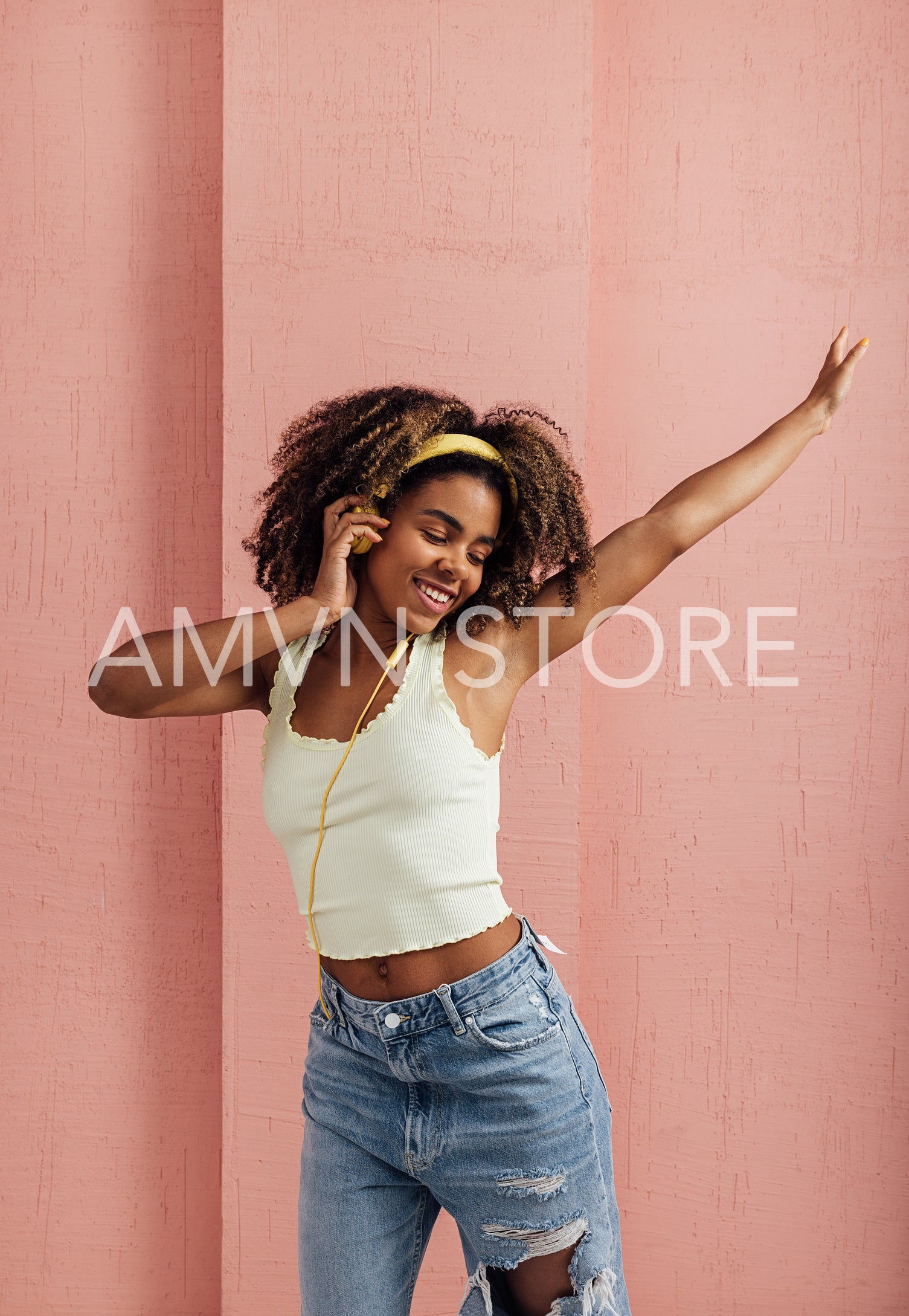 Young female having fun at pink wall. Woman wearing yellow headp