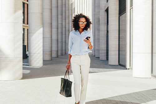 Businesswoman looking at smartphone while walking at modern office building