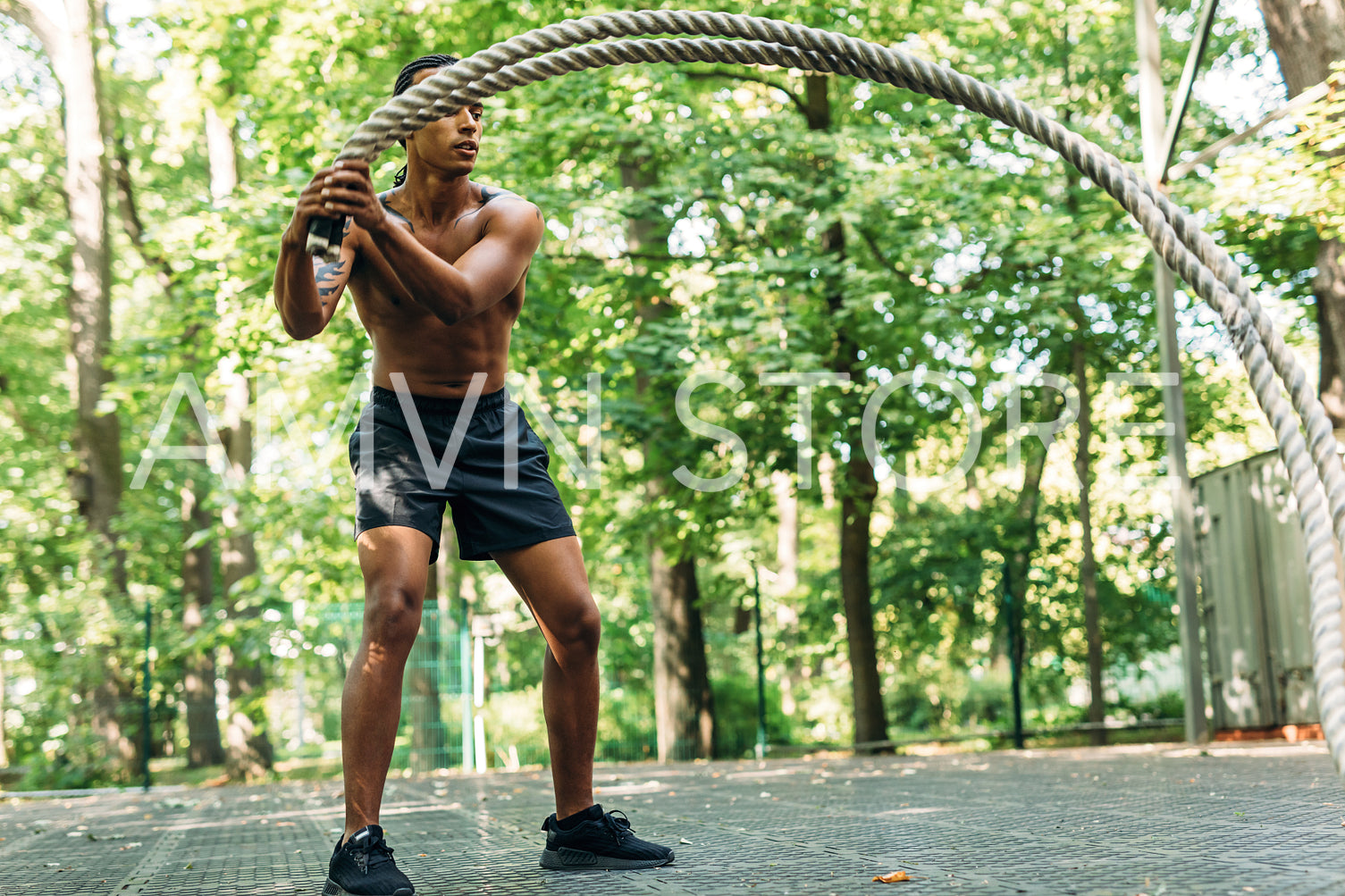 Bare chested muscular man doing workout using two battle ropes on sports ground	