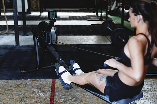 Sporty woman doing cardio workout on rowing machine in fitness club