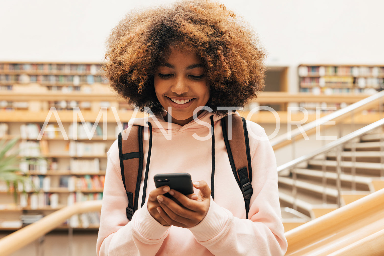 Close up of smiling schoolgirl standing in library and using smartphone