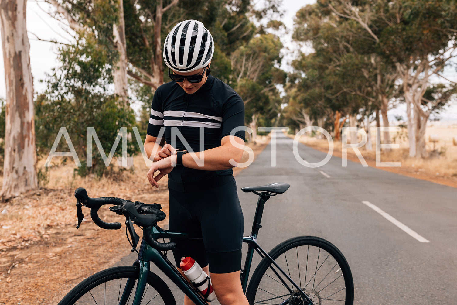 Young cyclist woman in sportswear checking smartwatch during training on countryside road