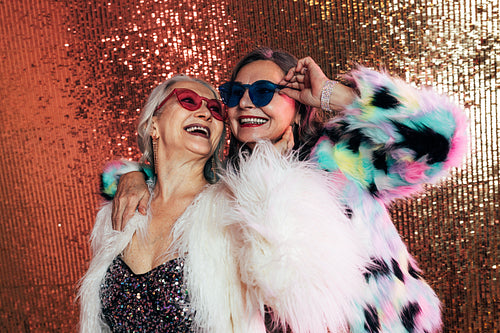 Two women wearing eyeglasses and fur coats. Senior females laugh