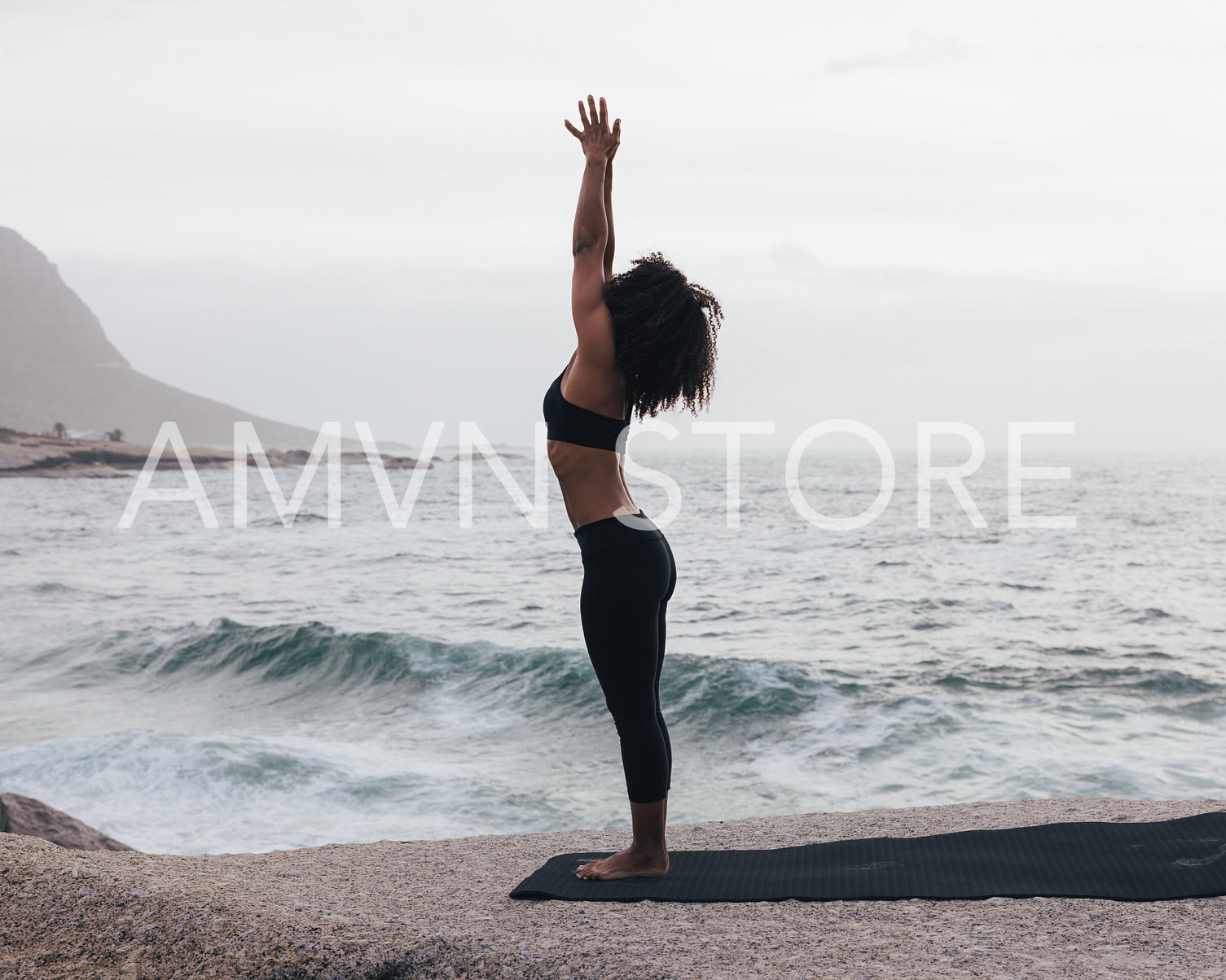 Woman practicing Urdhva Hastasana pose by ocean. Slim female standing outdoors in Raised Hands Pose.