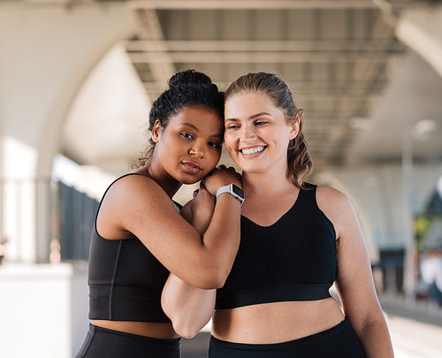 Two plus-size female friends in sportswear are standing together outdoors. Young women relaxing after intense workout hugging each other.