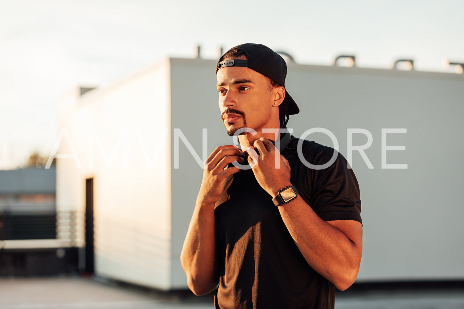 Confident male athlete standing on the roof at sunset and looking away