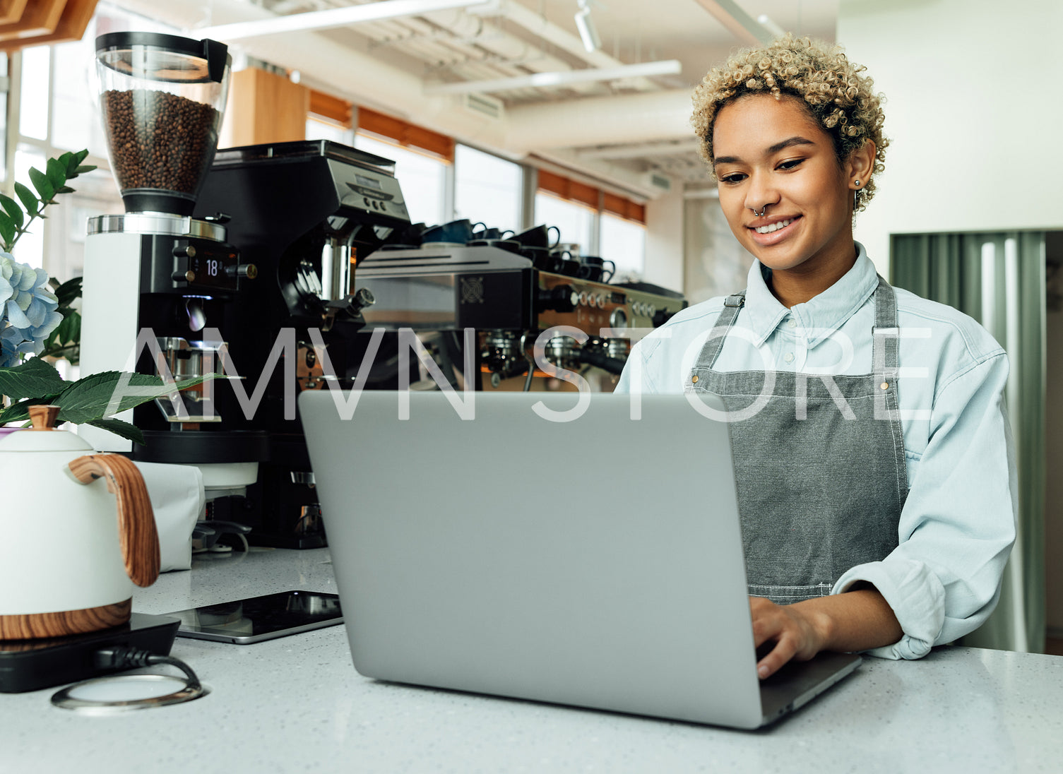 Smiling barista in apron typing on laptop in a coffee shop at the counter. Cafe owner working on a laptop.