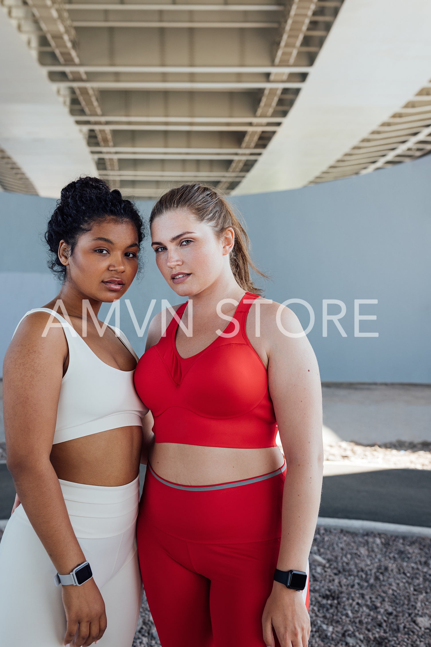 Portrait of two plus-size female athletes standing outdoors and looking at camera. Two young females in fitness attire standing together.