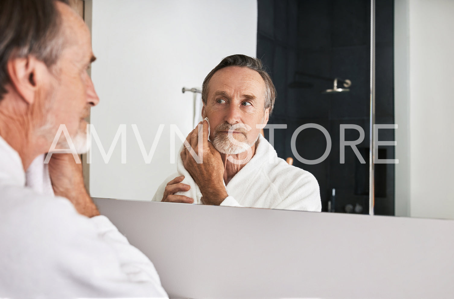 Senior man wiping his face with a towel in front of a mirror in bathroom	