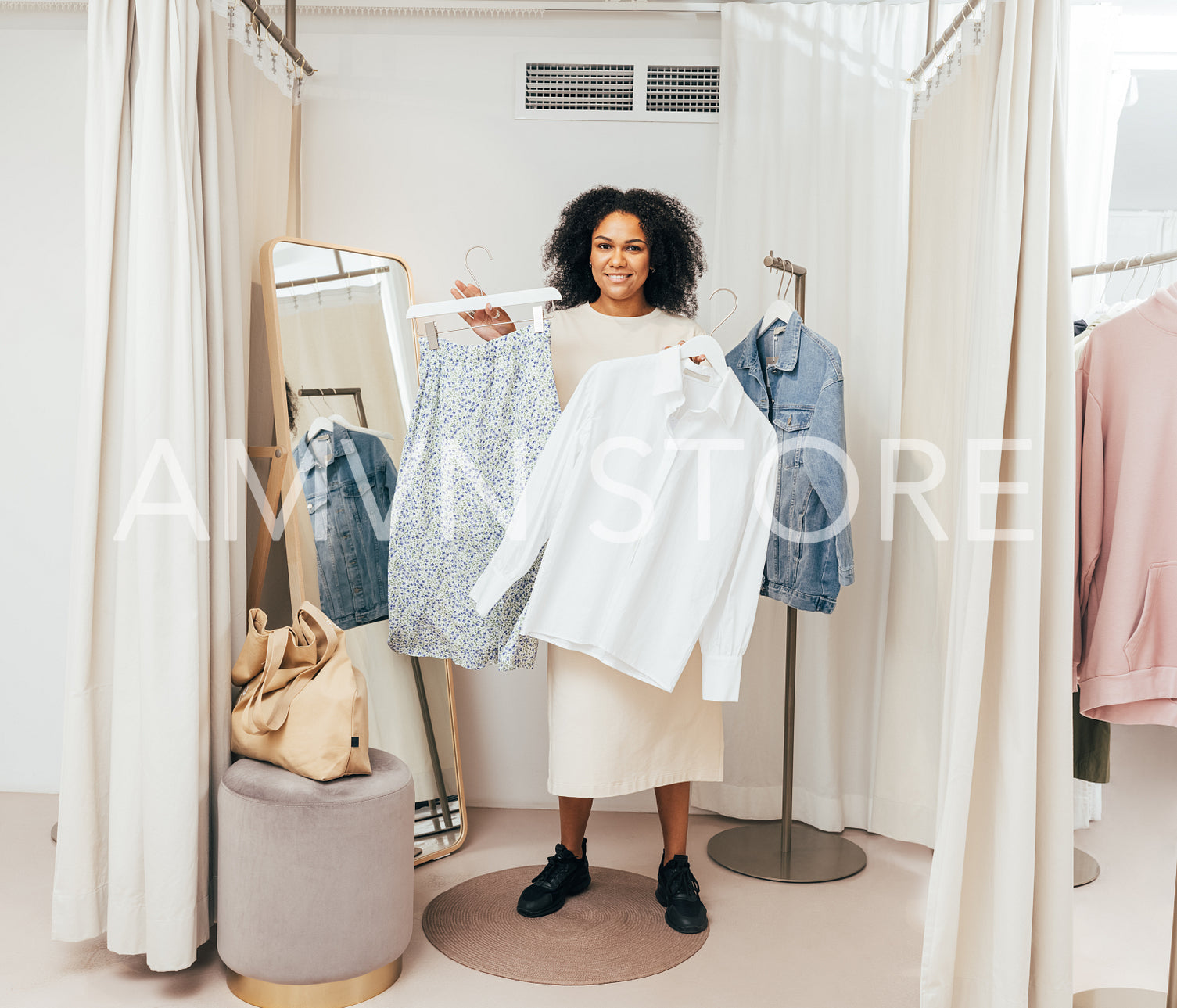 Stylish woman in fitting room standing with hangers looking at camera