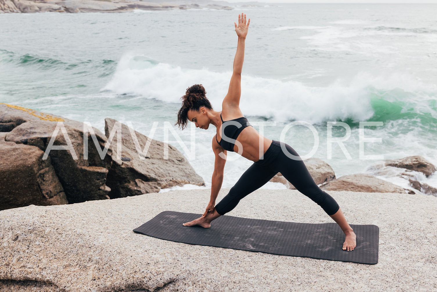 Full length of fit woman practicing yoga against beautiful view on ocean and waves. Slim female in fitness clothes stretching body outdoors.