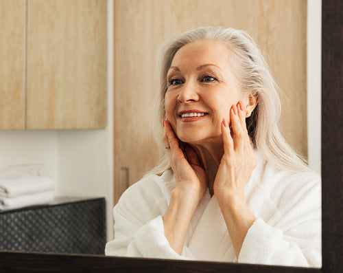 Woman with grey hair examines her face