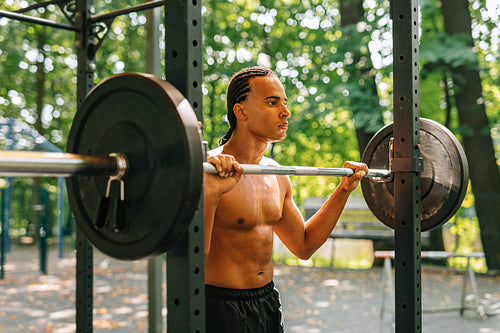 Young man leaning over weight bar after training outdoors