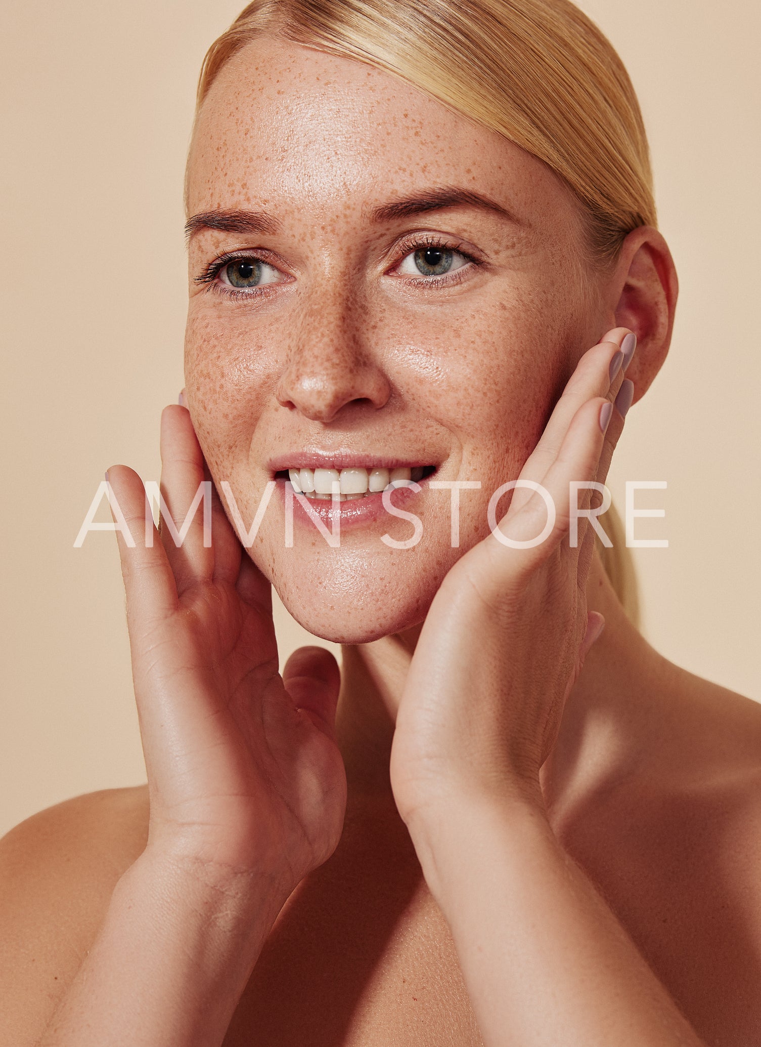 Highly detailed portrait of a young smiling woman massaging her face. Close up of blond female touching her freckled skin.