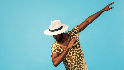 Young stylish guy in straw hat dancing in studio over blue background