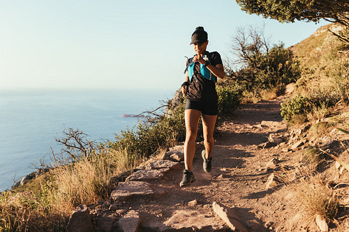 Fit woman running on the mountain trail. Female athlete in sportswear practicing cross country running.