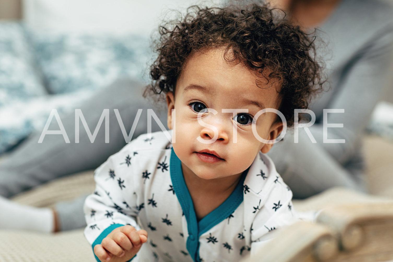 Close up portrait of a curly-haired baby boy crawling on bed	