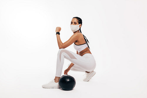 Young woman with face mask doing fitness workout with a medicine ball in studio