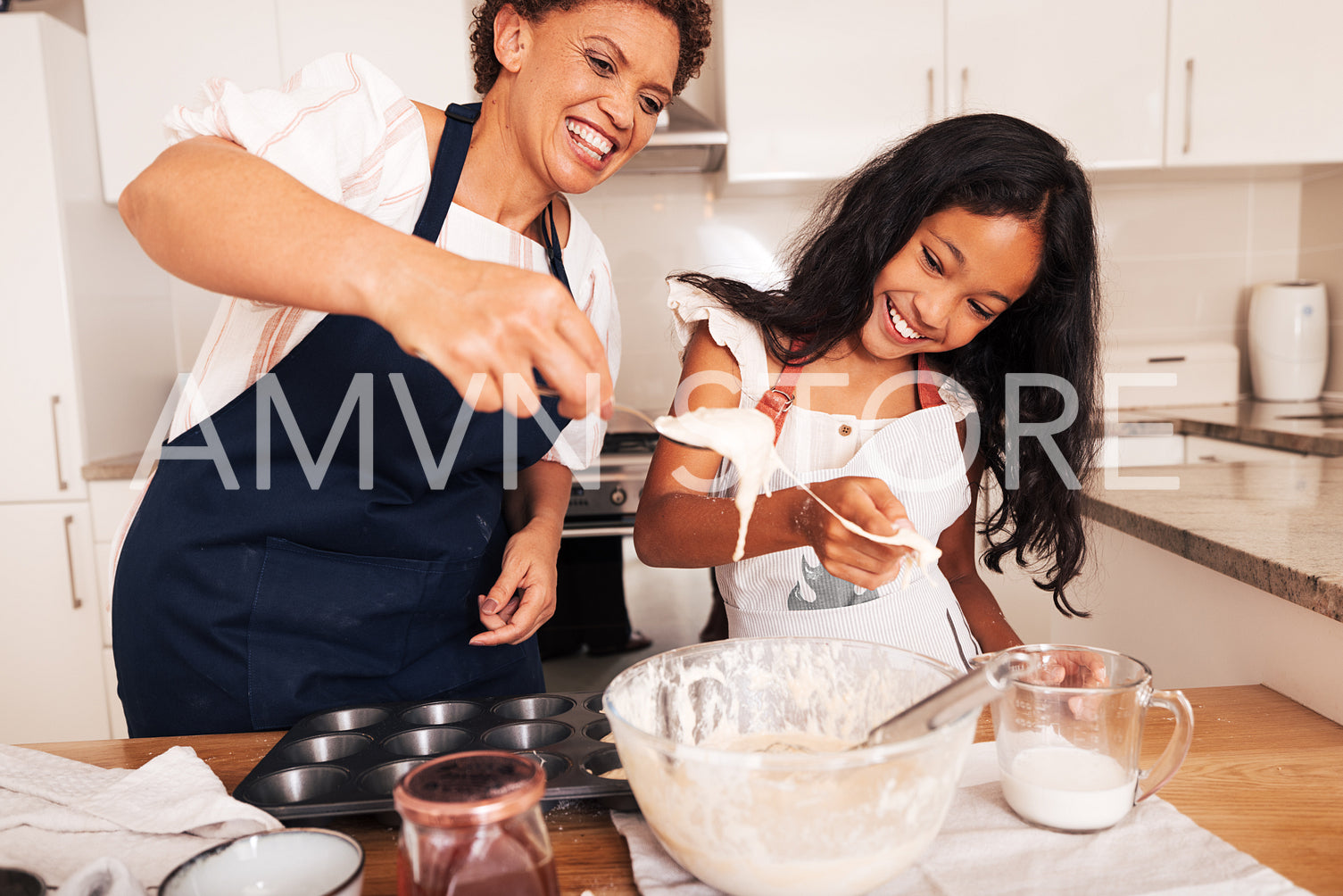 Girl and her grandmother are having fun while mixing dough in the kitchen. Smiling granny and a kid cooking together.