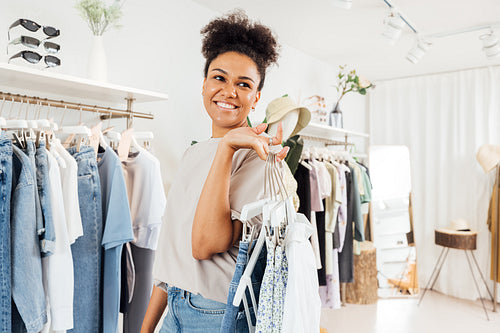 Young fashion store owner carrying clothes on hangers for arranging