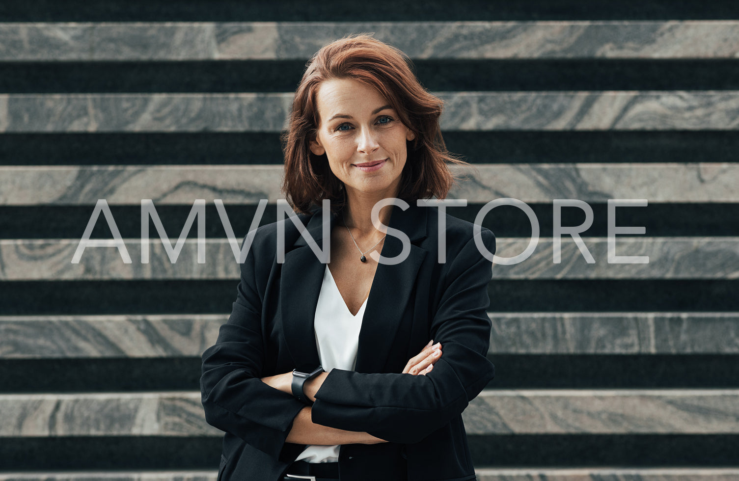 Smiling and confident middle-aged female with crossed hands. Businesswoman in black formal clothes with ginger hair.