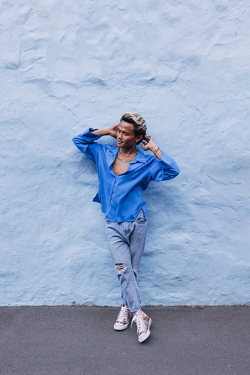 Guy in a blue shirt leaning wall outdoors. Full length of a young handsome man relaxing at a blue wall.