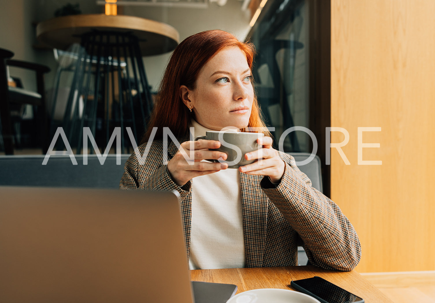 Thoughtful woman with ginger hair holding a cup of coffee sitting in a cafe looking at window