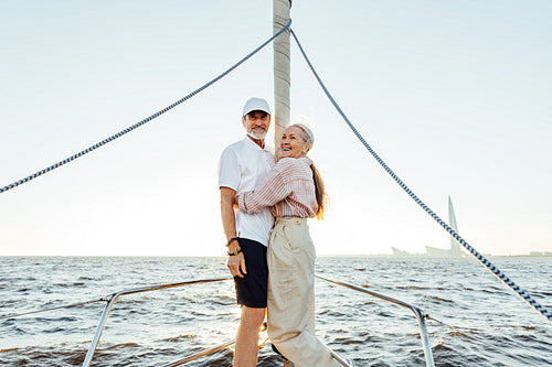 Two elderly people in casuals standing on yacht bow and smiling