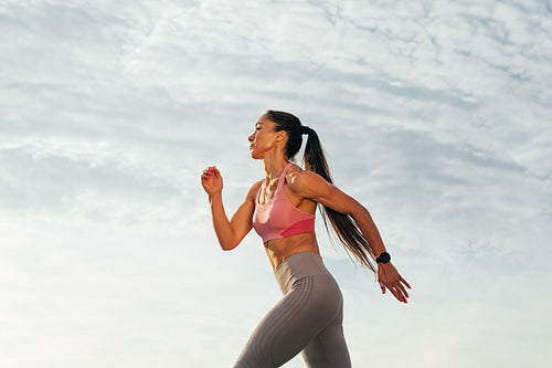 Sportswoman with long hair running outdoors against skies. Slim female jogger running on the rooftop.